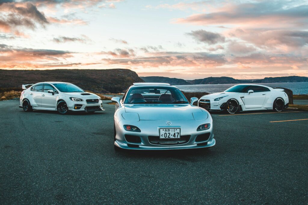 Three luxury sports cars parked outdoors with a stunning sunset backdrop.